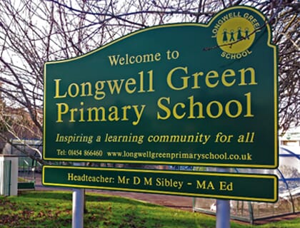 A green post mounted sign for a school